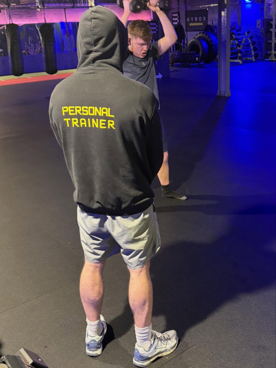 A trainer watching a person lift a weight in a gym